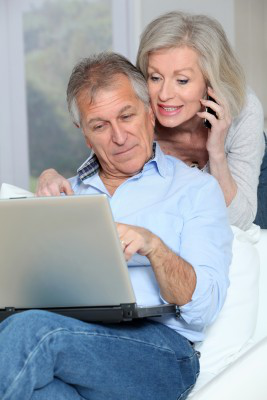 Dojrzali małżonkowie patrzą do laptopa. Kobieta trzyma w ręce słuchawkę od telefonu.