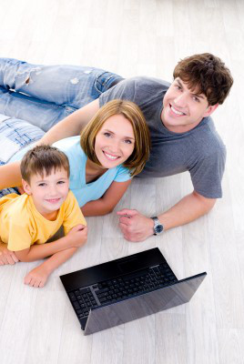 Rodzina - tata, mama i kilkuletni syn leżą na podłodze przed laptopem.